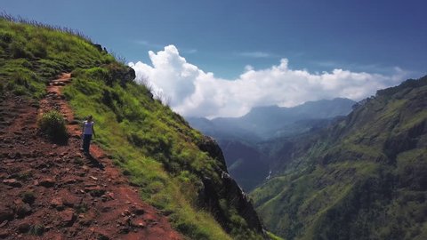 Woman walks on the mountain trail lying on the edge of the cliff with stunning valley views. The place named Little Adam's Peak in Ella, Sri Lanka