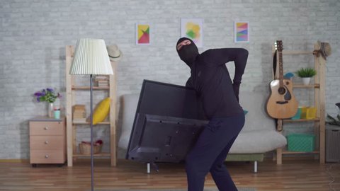 anonymous thief in a Balaclava mask stealing TV in the house and experiencing back pain injury