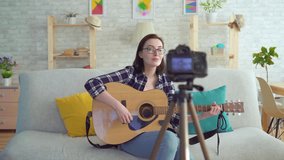 young woman blogger sitting on the couch with a guitar in his hands in front of the camera