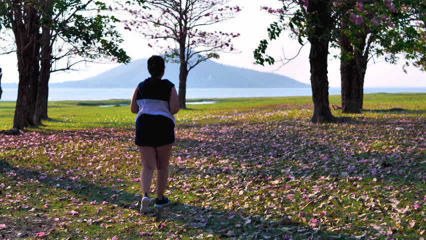 Over weight Asian woman jogging in natural sunlight in the evening, along with his son riding a bicycle.  exercising for good health. Slow Motion