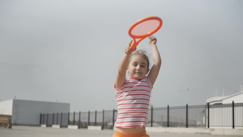 Little girl with tennis racket and ball in sport club. Active exercise for kids. Summer activities for children. Child learning to play tennis . Happy 7 year old girl jumping. Slow motion. 