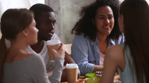 Diverse students multi-ethnic group of best friends sitting round the table in cafeteria chatting hanging out spending weekend, friendship between multi-racial adolescent, good warm relations concept