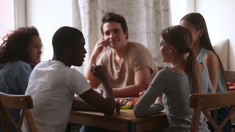 Rear view african guy sitting around the table with multi-ethnic friends telling story hang out with diverse millennial students enjoy free time with guys and girls drink coffee chatting in cafeteria