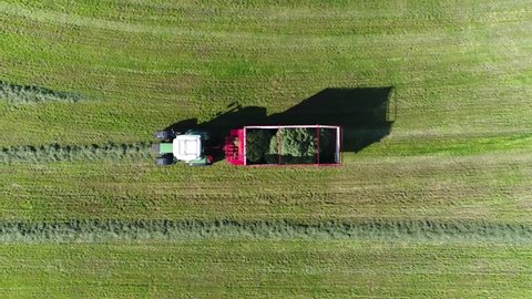 Aerial top down drone view of  green tractor pulling chaser bin picking up dried grass used as feed for livestock like cattle  in winter time typical modern farm scene 4k high resolution footage