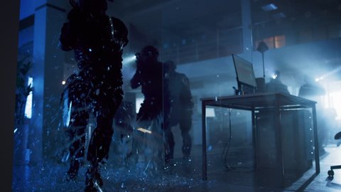 Masked Squad of Armed SWAT Police Officers Storm a Dark Seized Office Building with Desks and Computers. Soldier Breaks a Glass with His Arm and Team Continue to Move and Cover Surroundings.