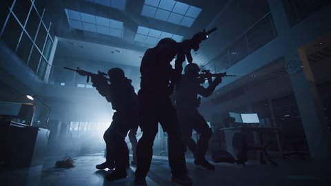 Masked Squad of Armed SWAT Police Officers Slowly Move in a Hall of a Dark Seized Office Building with Desks and Computers. Soldiers with Rifles and Flashlights Surveil and Cover Surroundings.