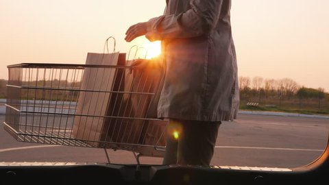Woman's silhouette, opens the trunk of a car, puts there paper shopping bags
