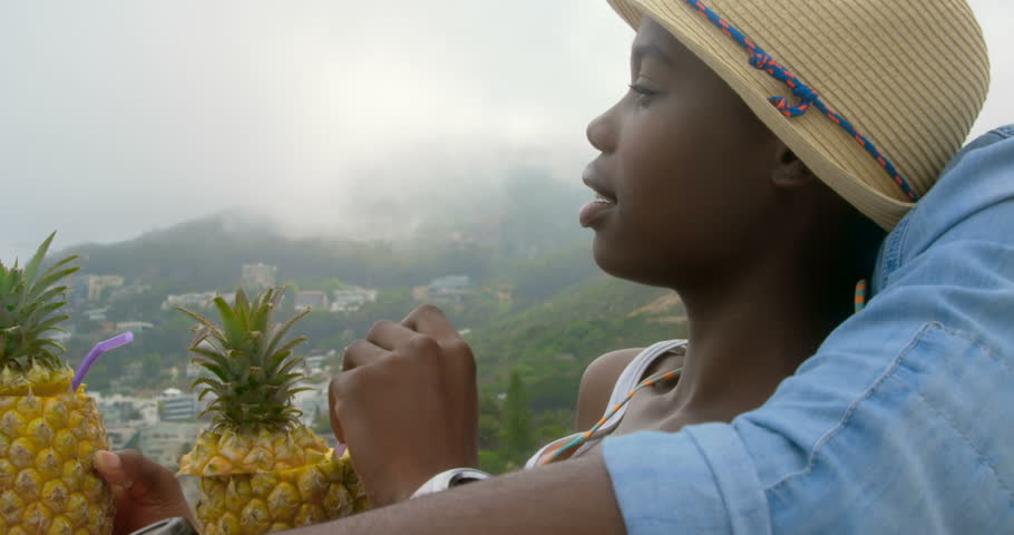 Side view of African american couple relaxing on the beach. They are drinking pineapple juice 4k