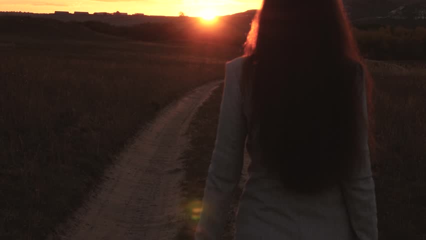 A business woman walks along a country road with a tablet in her hand, the sun miertsaet between women