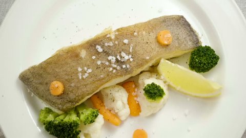 Fried halibut. A fillet of turbot on white plate with carrot, broccoli, cauliflower and slice of lemon. Slow motion. HD