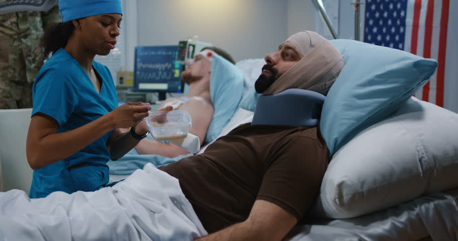 Medium shot of a nurse feeding injured soldiers in hospital bed
