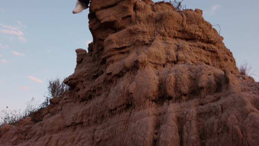 Young girl dressed in pink with black pants is sitting on a boulder on top of a precipice in the mountains. Leg that swing.
