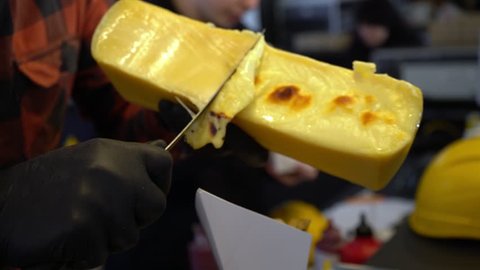 Scraping melted traditional Swiss Raclette cheese. Chef in black gloves scrapes cheese with a knife. Swiss cheese. Cooking