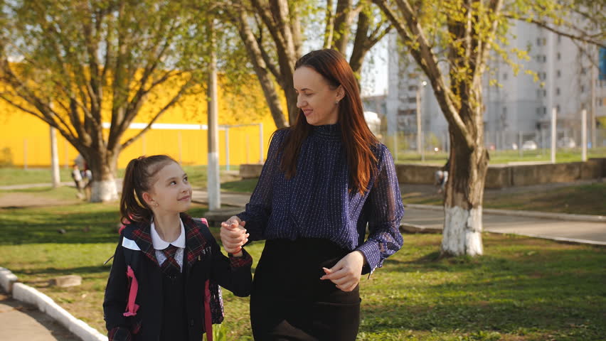 Mother is walking little girl in a school uniform to school. Mother and daughter together holding hands going to school.