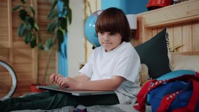 Sad cute boy sitting on bed hold laptop take toy cheerless childhood young online leisure internet kid technology communication computer education game slow motion