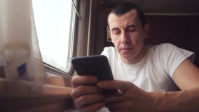 man businessman with smartphone travelling by train. man traveler is typing a internet web message in a train on the railway en route sits by the window of a carriage. slow motion video. interior