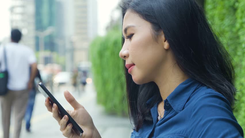 Side view of attractive young woman using a mobile phone while standing on the sidewalk. Shot in 4k resolution | Shutterstock HD Video #1028577971