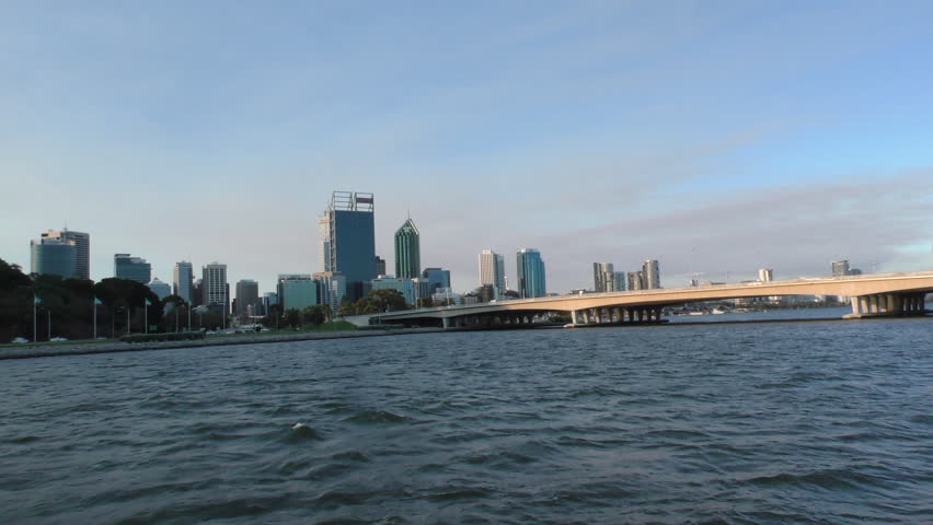 Panoramic slow motion scenic view of Perth skyline in Western Australia across the water of Swan River at sunset, from boat approaching the city.