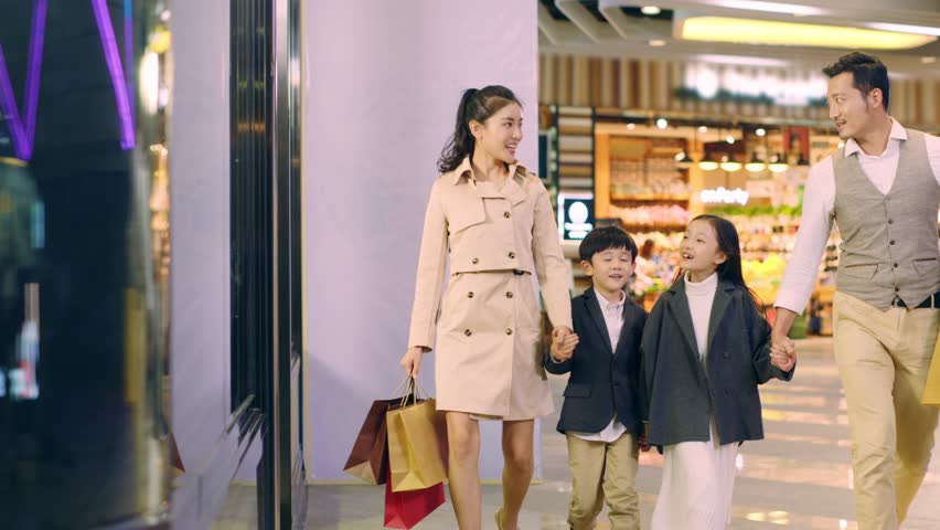 Happy asian family with two children walking hand in hand in shopping mall