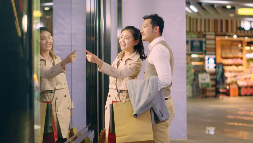 Happy asian couple shoppers walking in shopping mall 