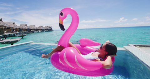 Flamingo Float Summer Vacation Woman in bikini on inflatable pink pool toy mattress in swimming pool. Elegant lady relaxing sunbathing enjoying travel holidays at resort pool. Luxury lifestyle.