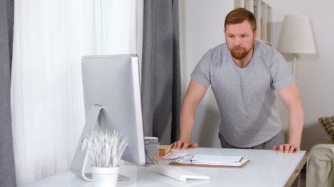 Tracking shot of athletic man in sportswear doing table push-ups at home and watching something on computer screen