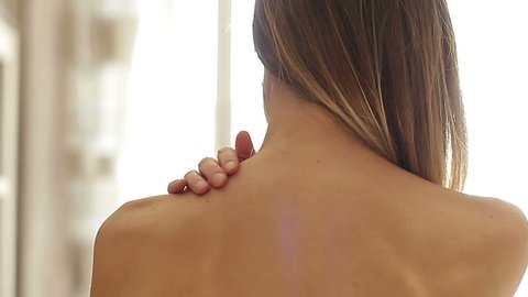 Blonde woman with long hair doing herself a neck massage shoulder rear view closeup