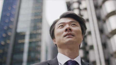 Professional Asian man in a suit looking around the city above him, in slow motion