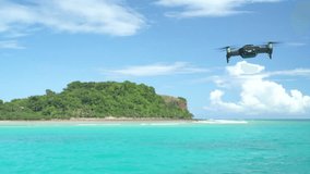 A drone hovers in place then flies towards a tropical island. Isolated drone.