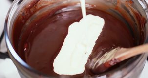 Closeup clip of melting dark, milk, and black chocolate in double boiler water bath bain-marie while adding condensed milk and stirring with a wooden spoon Sequence 3 of 4 4K 30 fps