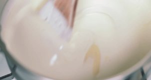 Slow Motion closeup clip of double cream and condensed milk in a saucepan being stirred with a wooden spoon to make a delicious cream 4k 60 fps