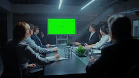 Late at Night In Corporate Meeting Room: Board of Directors, Executives and Businesspeople Sitting at Negotiations Table, Talking and Using Green Mock-up Screen Wall TV for Video Conference Call