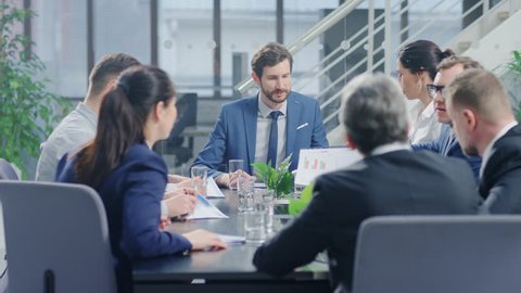 In the Modern Corporate Office Meeting Room: Diverse Group of Businesspeople, Lawyers, Executives and Members of the Board of Directors Talking, Negotiating, Use Documents and Consult Statistic Graphs