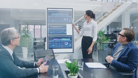 In the Corporate Meeting Room: Female Analyst Uses Digital Interactive Whiteboard for Presentation to a Board of Executives, Lawyers, Investors. Screen Shows Company Growth Data with Animated Graphs