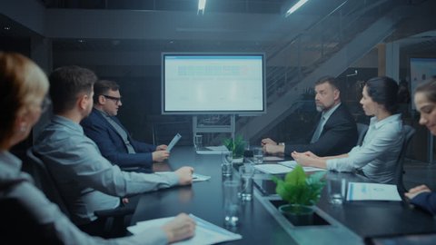 In the Modern Corporate Office Meeting Room: Diverse Group of Businesspeople, Lawyers, Executives Talking, Negotiating. They Consult Use Digital Whiteboard with Infographics and Use Documents