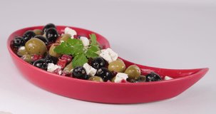 Reverse speed up closeup clip of lady picking up an olive from a beautiful arrangement of olives, feta cheese, red peppers, and parsley, with olive oil in a red Tear Drop Shaped Plate 30 fps 4K