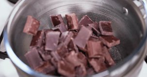 Reverse closeup clip of dark, milk, and black cooking chocolate being poured into a bowl in double boiler water bath bain-marie to cook a pave french dessert 4K 30 fps