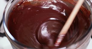 Closeup clip of melting dark, milk, and black chocolate in double boiler water bath bain-marie while adding condensed milk and stirring with a wooden spoon 