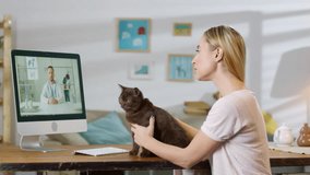 Sequence of shots of woman sitting at table and petting cat while talking on video call with male veterinarian giving her online consultation