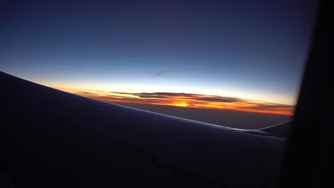 Sunset from the airplane window. View of the orange sun, aircraft wing, dark sky and clouds. The bright orange of the setting sun. View from the plane window. Above the clouds. Long wing.