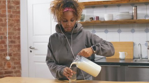 Beautiful young African-American woman having breakfast with milk in the kitchen after morning jogging