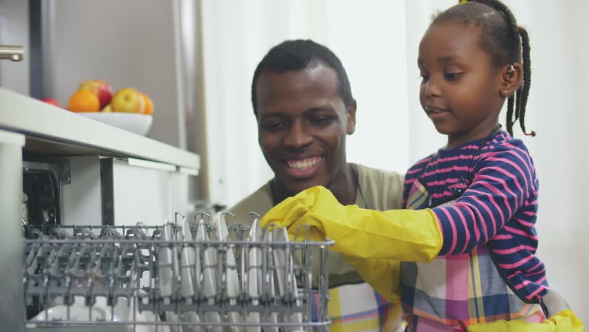 Pretty Afro-American little girl and her father emptying the dishwasher in the kitchen Royalty-Free Stock Footage #1028621537
