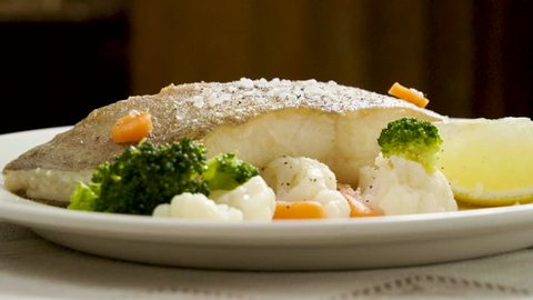 Fried halibut. A fillet of turbot on white plate with carrot, broccoli, cauliflower and slice of lemon. Slow motion. HD
