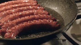 In the hot oil in a frying pan the cook is laying sausages. Close-up, slow motion, 4K UHD video.