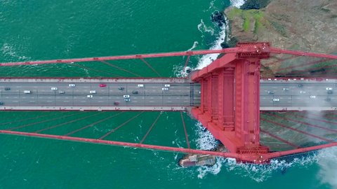 Aerial video of the Golden Gate. The busy road on the red bridge over the deep green Pacific Ocean. Fog drifting above the waves crashing the San Francisco Slow motion. California USA. Top view 4K