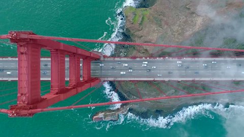Aerial view of the Golden Gate Bridge. Cloudy fog soaring above the traffic on the red bridge over the green waters of the Pacific Ocean. San Francisco Bay, California, USA. Drone video