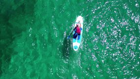 Aerial view video of unidentified fit woman on sup or stand up paddle surf board in tropical caribbean turquoise seascape