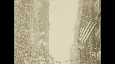 1920s: Ticker tape parade in New York City with the street a foot high in paper and streamers. View of parade from street. Policemen hold crowd back.