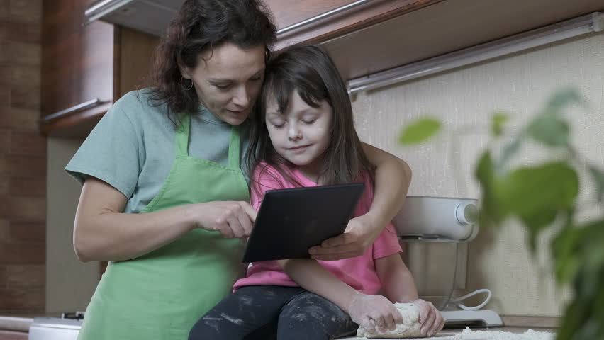Woman with a child in the kitchen. Mother and daughter looking for recipes for the issue in the Internet.