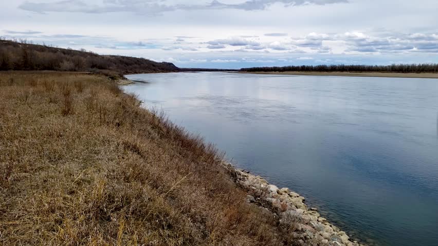 Missouri river gently flowing past early spring pasture. Gentle breeze rustling prairie grass in foreground.
